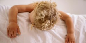 un enfant blond qui dort sur son lit en été