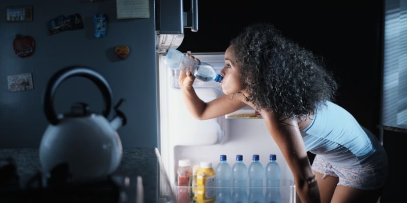 femme qui boit de l'eau glacé car elle a chaud la nuit