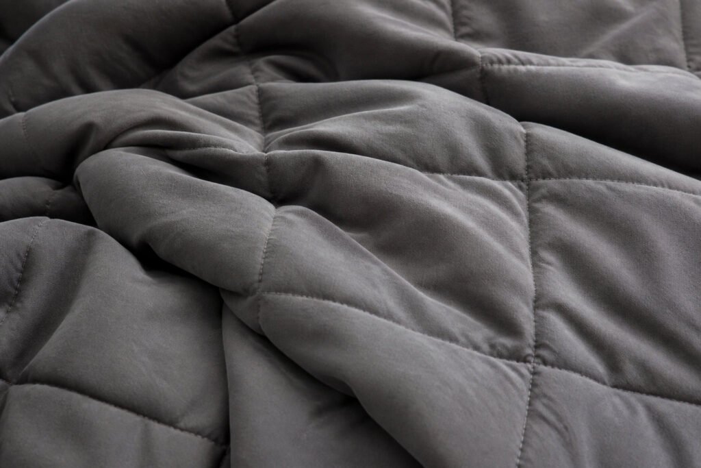 Gros plan sur les plis et les coutures matelassées en losanges d'une couverture lestée de couleur gris anthracite.